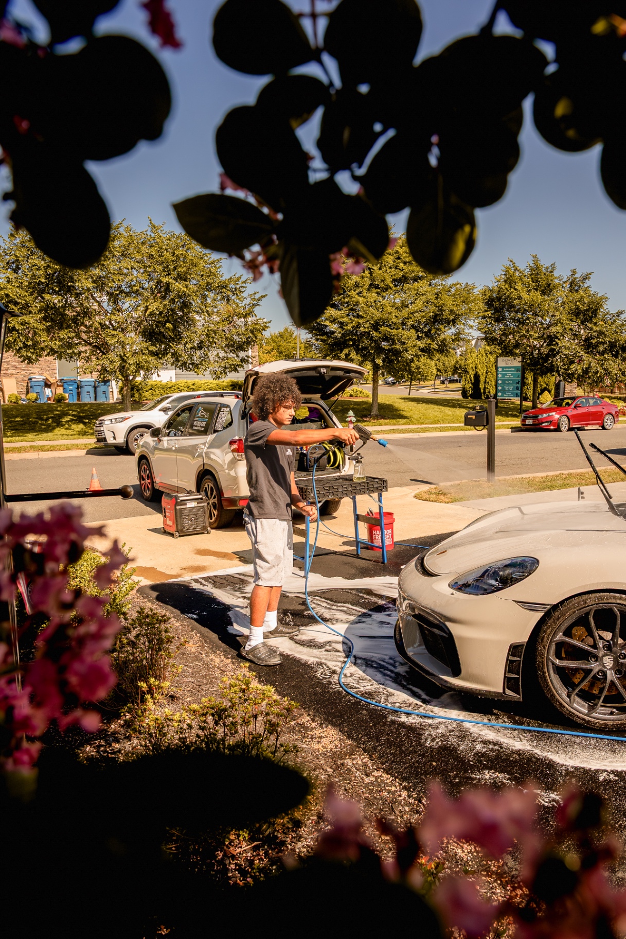 Dominick of Slums Mobile Detailing pressure-washing a white Porsche in a customer's driveway