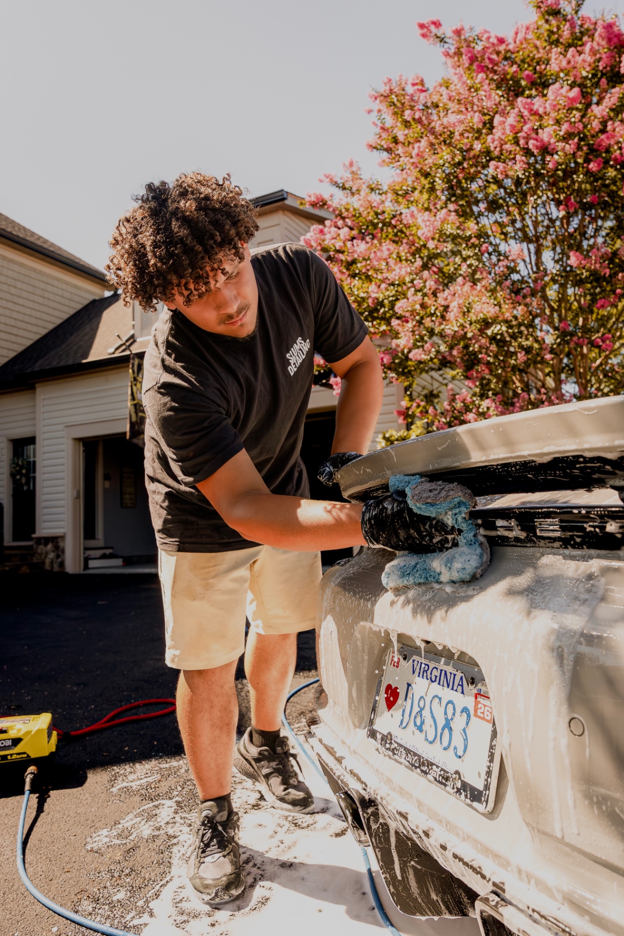 Hand-washing soap over the rear bumper and Virginia plate of a sports car during a mobile detail